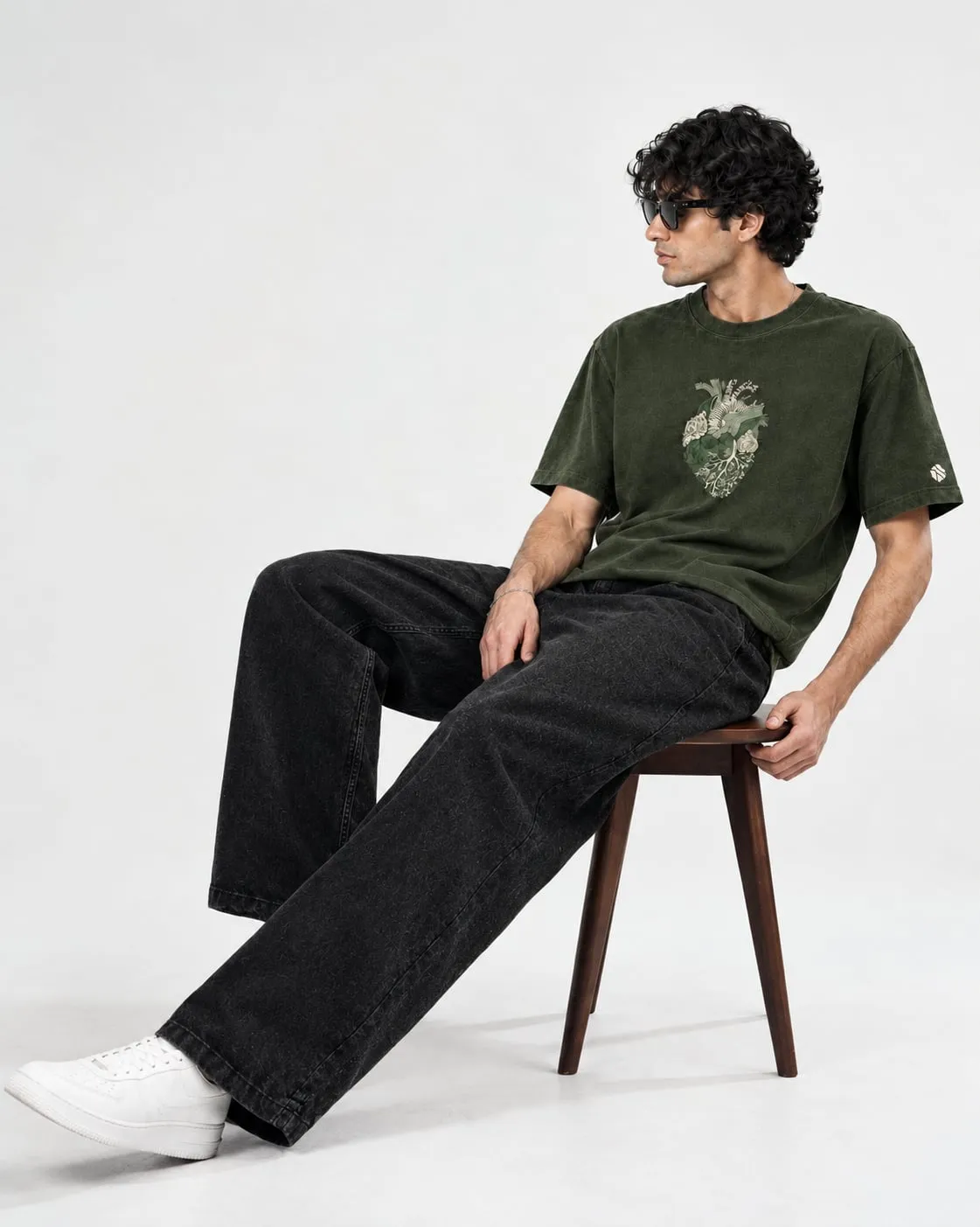 Model seated on a wooden chair, wearing Olive Grove with black wide-leg denim